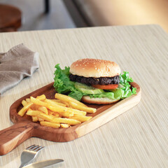 A mouthwatering burger topped with fresh vegetables sits next to crispy fries on a rustic wooden platter in a warm café atmosphere