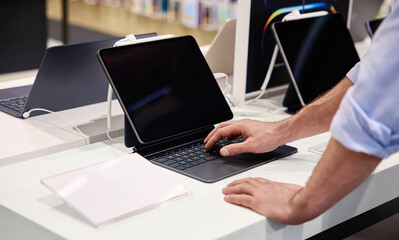 A user interacts with a tablet in a tech store displaying various electronic products