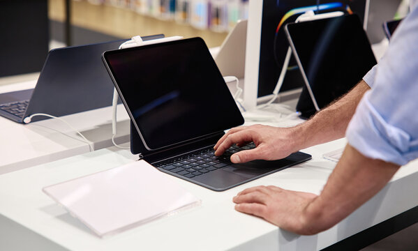 A user interacts with a tablet in a tech store displaying various electronic products