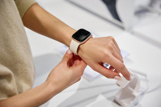 A woman is attempting to try on a stylish and modern smartwatch in a retail store setting
