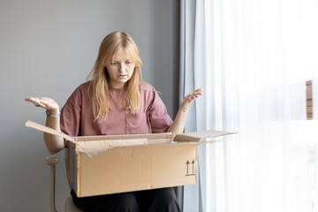 Unhappy young blonde woman frustrated by wrong order shopping online. Upset female buyer unbox...