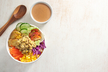 Salad, A vibrant bowl filled with quinoa, lettuce, carrots, cucumbers, corn, and tomatoes sits next to creamy dressing on a wooden spoon