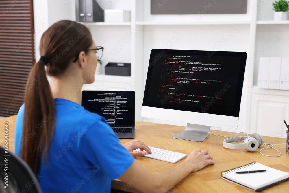 Poster programmer working on laptop and computer at wooden desk indoors, back view