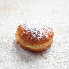 A soft, round donut dusted with powdered sugar is placed on a rustic wooden surface, evoking a warm breakfast atmosphere