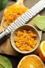 Orange zest, grater and fresh fruit pieces on wooden table, flat lay