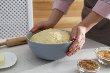 Making cinnamon rolls. Woman with dough at white wooden table, closeup