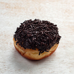 A freshly baked donut with a thick layer of chocolate sprinkles sits on a rustic wooden table, inviting for a tasty treat