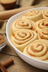 Raw cinnamon rolls in baking dish on wooden table, closeup
