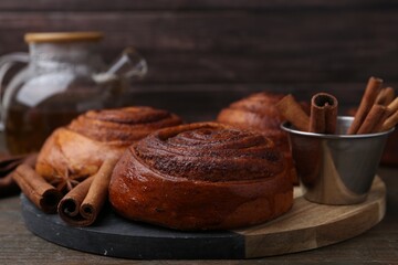Delicious cinnamon roll buns and spices on wooden table, closeup