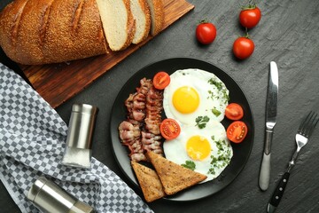 Tasty brunch. Delicious fried eggs, bacon and pieces of toast served on black table, flat lay