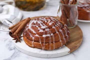 Tasty cinnamon roll with cream and spices on white marble table, closeup