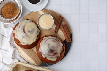Tasty cinnamon rolls with cream, spices and coffee on white tiled table, flat lay. Space for text