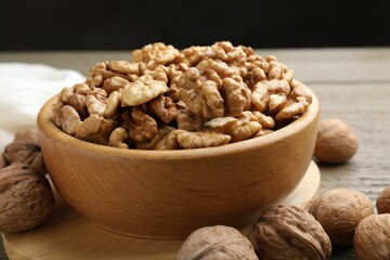 Peeled walnuts in bowl and whole ones on wooden table, closeup