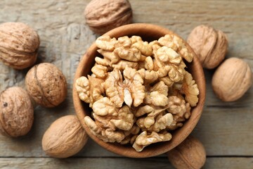 Peeled walnuts in bowl and whole ones on wooden table, flat lay
