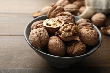 Fresh walnuts in bowl on wooden table, closeup