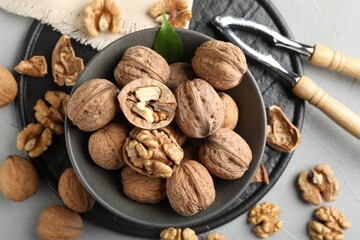 Fresh walnuts in bowl and nutcracker on gray table, flat lay