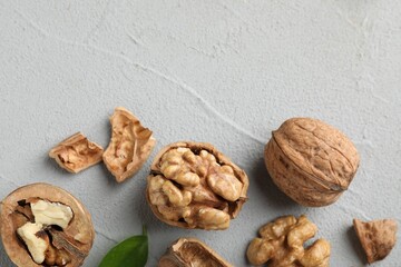 Fresh walnuts with shells on gray textured table, flat lay. Space for text
