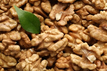 Pile of fresh ripe walnuts and green leaves as background, top view
