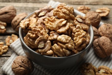 Shelled walnuts in bowl and whole ones on table, closeup