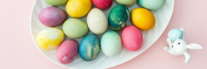 Multi-colored Easter eggs in an oval dish with decorative bunnies on a pink background, Happy Easter holiday