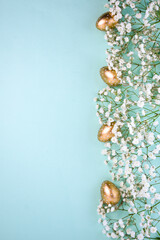 Golden Easter eggs with white polka dots and delicate white gypsophila flowers on a pastel...