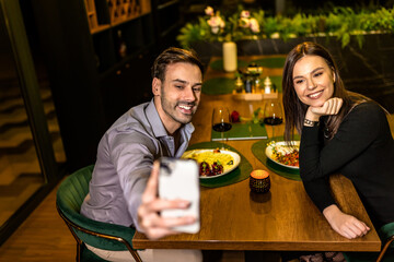 Young, happy beautiful couple taking selfie on a romantic dinner date at the restaurant.