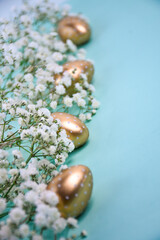 Golden Easter eggs with white polka dots and delicate white gypsophila flowers on a pastel...