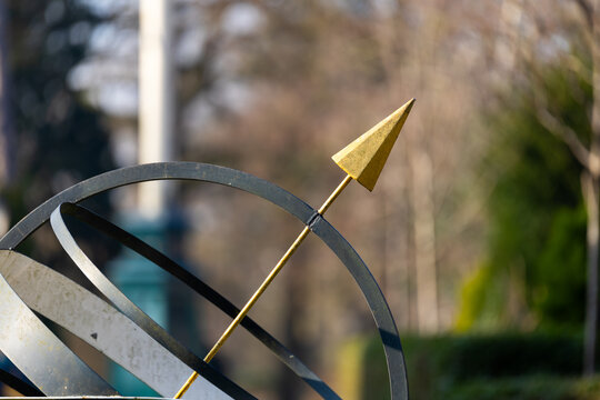 Close-Up of a Metal Armillary Sphere Sundial with a Golden Arrow in a Garden Setting