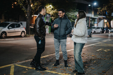 A group of friends engaged in a casual, cheerful conversation outdoors in an urban area at night, showcasing friendship and leisure in a lively, modern city setting.