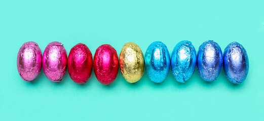 Row of chocolate Easter eggs in foil on color background