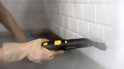 Housekeeper cleaning white tile grout with steam cleaner in kitchen