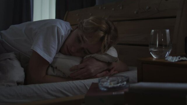 Upset young woman leans on pillow hugging tight in bed