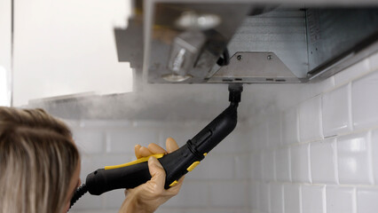 Housekeeper cleaning kitchen extractor hood with steam cleaner