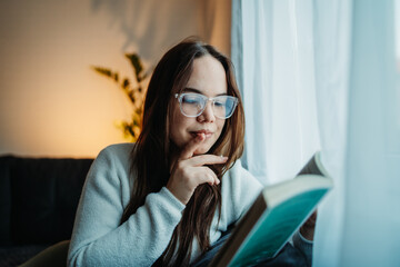 Young caucasian woman reading book or learning by the window	