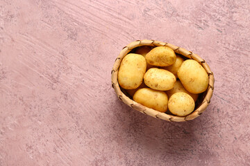 Wicker basket with raw baby potatoes on pink background