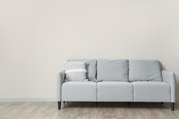 Grey sofa with cushion near light wall in room