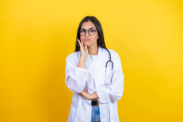 Young brunette doctor woman wearing stethoscope standing over isolated yellow background thinking looking tired and bored with crossed arms