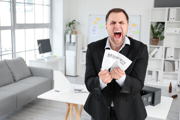 Angry businessman with papers in office. Bankruptcy concept