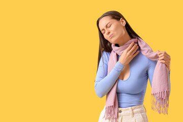Young woman in scarf suffering from sore throat on yellow background