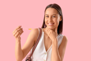 Young woman with syrup for sore throat on pink background