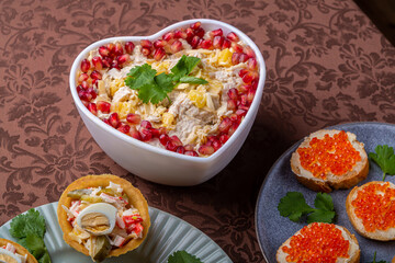 Salad with chicken, pineapple and pomegranate in a heart-shaped salad bowl next to tartlets