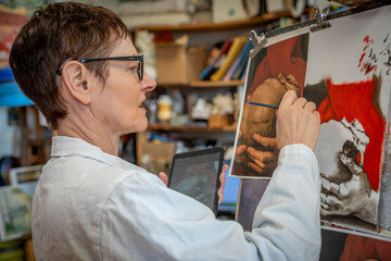 Paris, France - 02 01 2025: A mature woman with short hair and glasses paints a picture with oil paint during a drawing class.