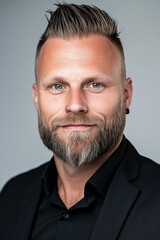 Confident man with a beard in a formal dark outfit posing against a neutral background