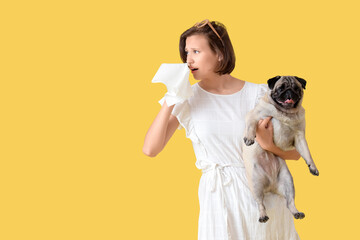Allergic young woman with cute pug dog on yellow background