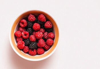 Bowl filled with ripe raspberries and blackberries on a light surface captures fresh fruit appeal