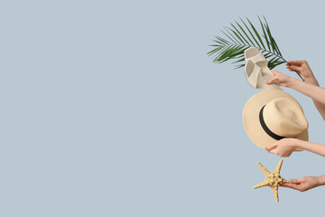 Hands holding sandals with hat, palm branch and starfish on blue background