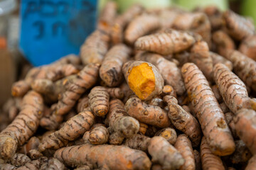 Turmeric roots stacked in a heap for sale at a stall. One is sliced in half.