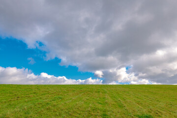 Idyllic nature background. Green grass summer meadow under the beautiful sky with clouds.