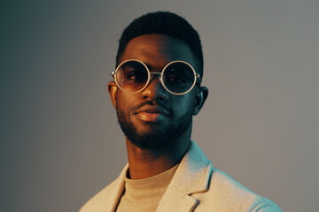 Fototapeta premium Stylish African man in modern eyewear, wearing a fashionable gray blazer and turtleneck, exuding confidence and sophistication against a gradient background