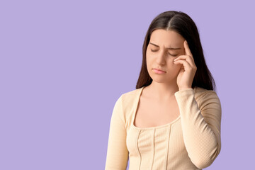 Young woman suffering from headache on lilac background